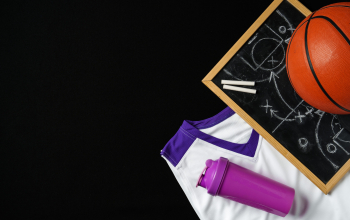 A basketball, along with a strategic play diagrammed on a chalkboard, rests near a folded jersey and a sports bottle. The equipment is arranged on a dark surface, suggesting preparation for a game or a coaching session in progress.
