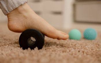 Woman doing flatfoot correction gymnastic exercise using massage roller. Myofascial relaxation of foot muscles. Hallux valgus. Pain. Identification of flat feet. Self care practices at home, health