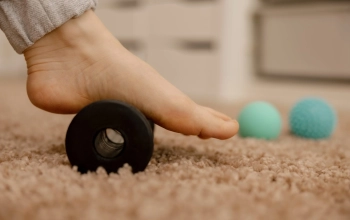 Woman doing flatfoot correction gymnastic exercise using massage roller. Myofascial relaxation of foot muscles. Hallux valgus. Pain. Identification of flat feet. Self care practices at home, health